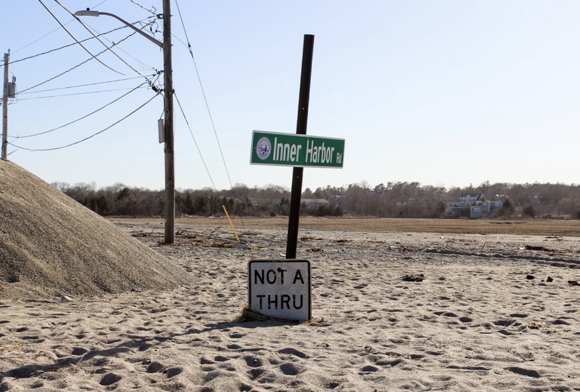 Inner Harbor Road sign and a Not a Thru sign half buried in sand